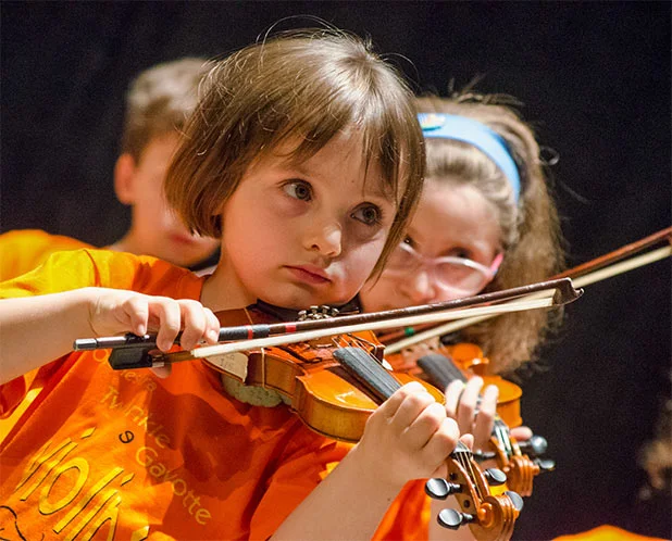 Bambina concentrata che suona il violino con l'archetto durante una lezione di violino con il metodo Suzuki