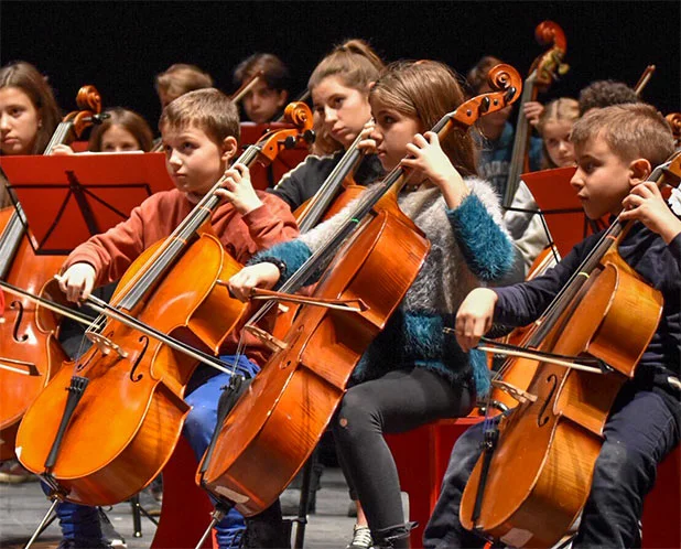 Giovani musicisti concentrati suonano il violoncello in orchestra, esperienza collettiva del percorso Suzuki per bambini a Torino.